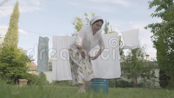 漂亮的高级妇女头上披着白色披肩在花园特写的绳子上挂着亚麻布洗衣日视频的预览图