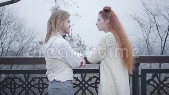 侧面看白种人年轻夫妇面对面站着说话在秋天公园约会的时髦男女视频的预览图