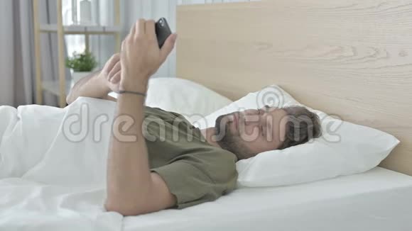 震惊的年轻人在床上用手机说话视频的预览图