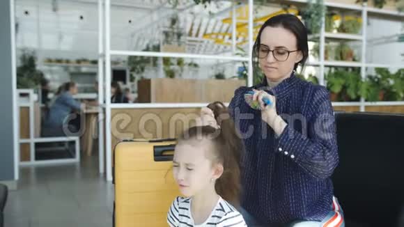 妈妈在机场大厅梳着一个脾气暴躁的女儿的头发视频的预览图