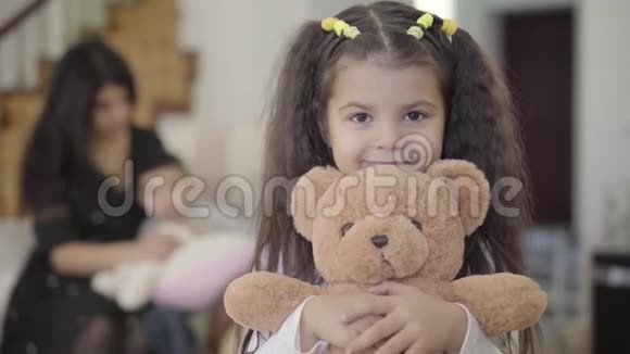 一个微笑的中东女孩棕色的眼睛和卷曲的头发抱着泰迪熊看着视频的预览图