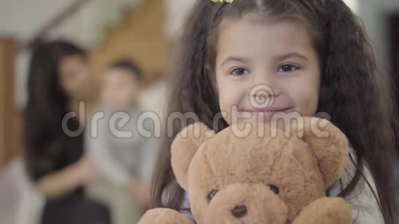 一个快乐的中东女孩的特写脸棕色的眼睛和卷曲的头发抱着泰迪熊微笑儿童视频的预览图