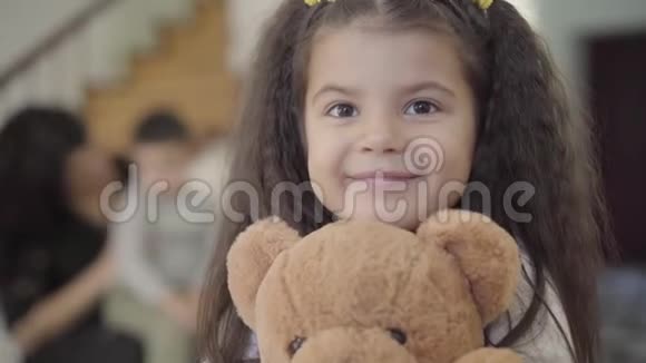 一个快乐的中东女孩的特写棕色的眼睛和卷曲的头发抱着泰迪熊微笑儿童视频的预览图