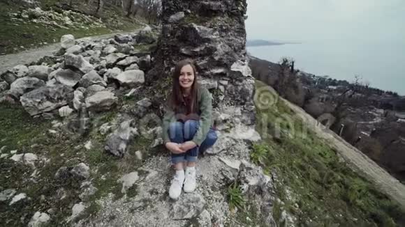 可爱的女孩坐在海边的一座山上的一座古老堡垒的墙边视频的预览图