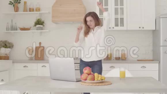开朗的白种人女孩穿着休闲服装在轻盈的现代厨房跳舞快乐的美女周末视频的预览图