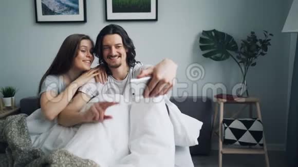 快乐的一对情侣在床上用智能手机拍照微笑着摆姿势视频的预览图