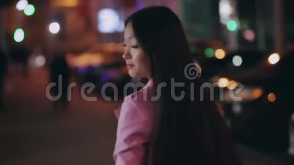 时髦的亚洲女人走在一个夜晚的城市里转脸回头看视频的预览图