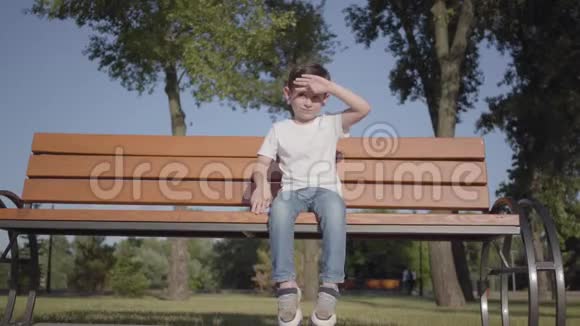 可爱的小男孩坐在公园的长凳上可爱的孩子独自呆在户外夏日休闲视频的预览图