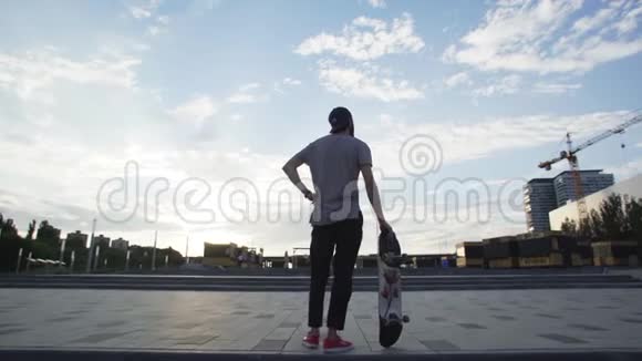 公园内滑板运动员站着滑板的后视图视频的预览图
