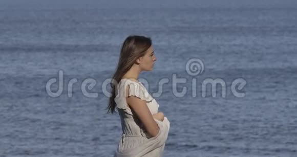 站在海浪背景下思考着一位穿着浅色白裙的白种人美丽女子的侧面景色视频的预览图