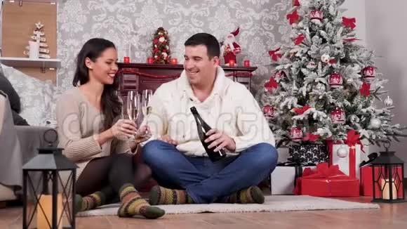 一对夫妇在圣诞节装饰的房间里坐在地板上喝香槟视频的预览图