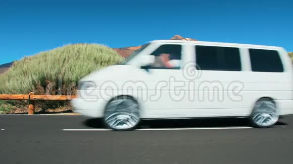 白色小型货车在沙漠中的一条山沥青路上行驶在火山峰的背景下明亮明亮视频的预览图