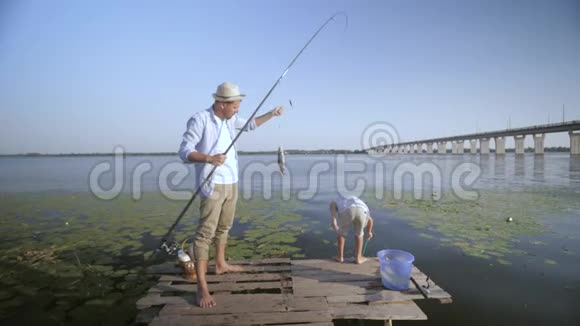 家庭活动快乐的父亲拿着鱼竿快乐的儿子在夏季周末在码头上快乐地钓鱼视频的预览图