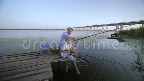 家庭周末在户外父亲和儿子在暑假期间在芦苇丛中水边的木桥上钓鱼视频的预览图