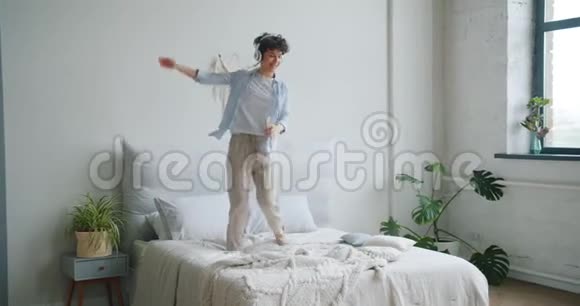 快乐的女士戴着智能手机在床上跳舞享受着音乐视频的预览图