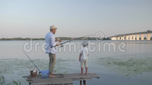 暑假在河边闲逛戴着草帽的快乐父子把鱼从水里拉出来视频的预览图