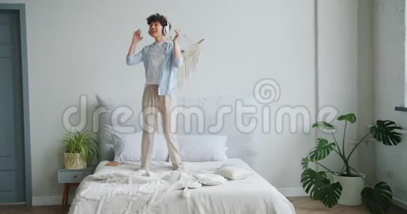 女人在床上跳舞的慢动作用耳机听音乐玩得开心视频的预览图