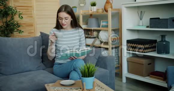 可爱的年轻女人在舒适的房子里看书和喝茶视频的预览图