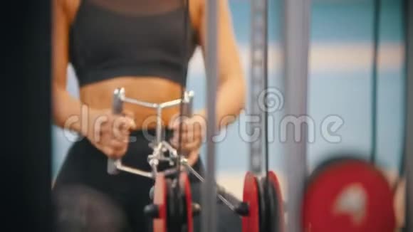 一个穿着运动服在健身房训练的运动女性拉着与重物相连的把手视频的预览图