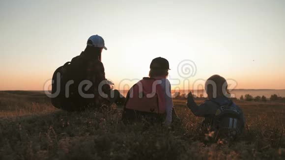 母亲和两个背包的孩子坐在山上的小径上他们喝水在旅途中放松视频的预览图