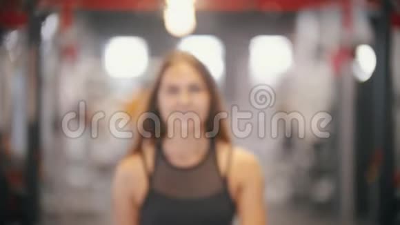 一位带着长发的运动员微笑的女子在健身房里喝水视频的预览图
