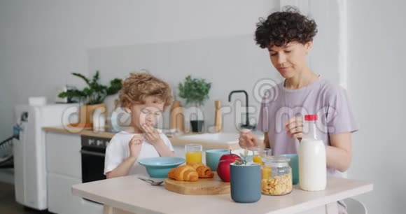 年轻女子喝橙汁而儿子则在餐桌上吃麦片视频的预览图