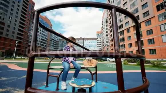 小女孩在公园操场上玩旋转木马夏天一个孤独的孩子在院子里骑着玩具的旋转木马视频的预览图