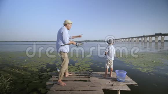 逗乐的父亲和儿子fisherm欢快的欢快的小男孩戴着草帽在码头的码头上钓鱼视频的预览图