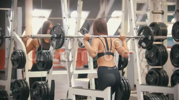一个在健身房训练的女运动员在哑铃下把它扛在肩上视频的预览图