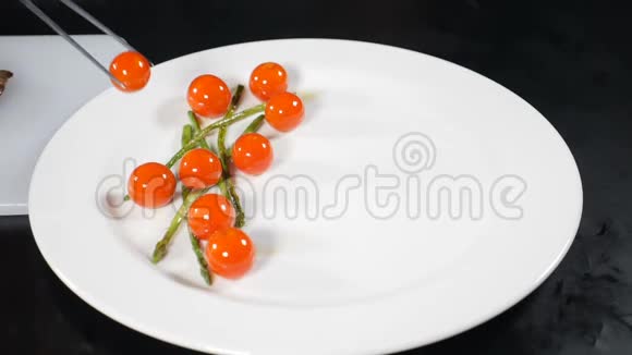 厨师在餐厅厨房做饭把番茄樱桃和芦笋用钳子放在白色盘子里做点菜好吧视频的预览图