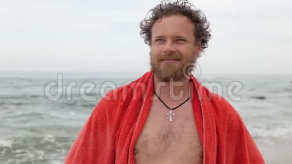 一个留着胡子的年轻人蓝色的眼睛盯着大海的背景肩膀上有一条毛巾微笑着看着镜头4视频的预览图