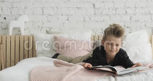 小男孩正在看一本纸书躺在卧室的床上在家门口看视频的预览图