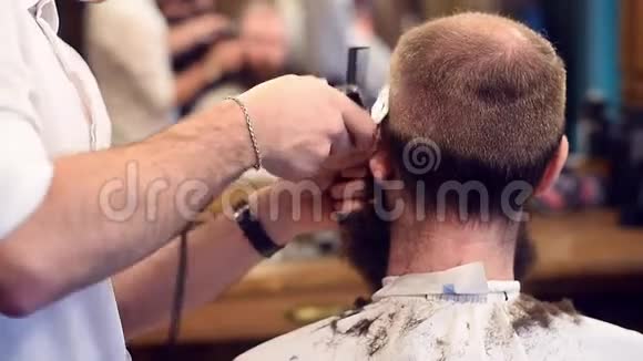理发师用电动剃须刀和梳子工作在理发店理发戴斗篷的人客户背面视频的预览图