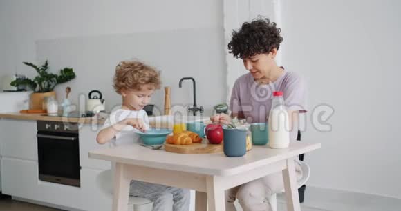 快乐的母亲和儿子在家边喝牛奶边吃麦片的慢动作视频的预览图