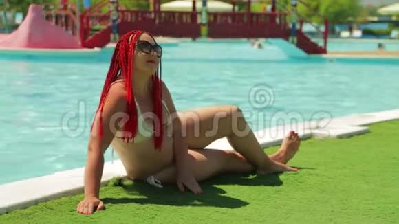 游泳池边的一位年轻的黑发女人穿着泳衣打日光浴视频的预览图