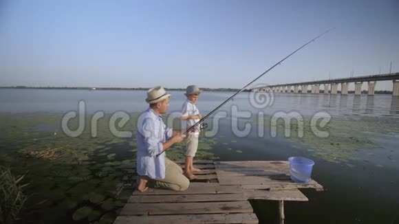家庭钓鱼有爱心的男性父母教他们的小儿子在河边的码头上旋转同时放松视频的预览图
