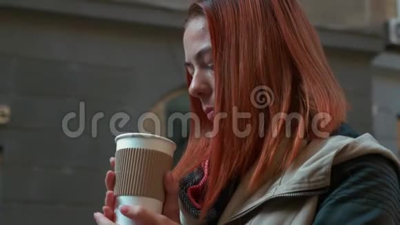 有着狐臭头发的女孩在街上的纸杯里喝茶视频的预览图