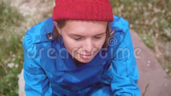 在阳光明媚的夏日里有趣的女孩戴着红帽子穿着蓝色外套的金发碧眼浑身湿透看着镜头笑眯眯的视频的预览图