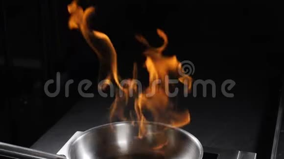 在黑暗的背景下从不锈钢煎锅中升起火焰煮火焰菜厨师准备火焰杯的特写视频的预览图