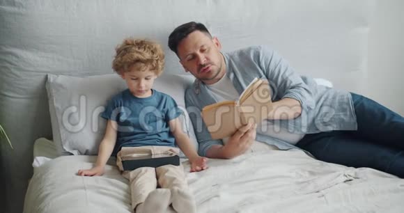 年轻的父亲在孩子睡觉时给小男孩读书视频的预览图