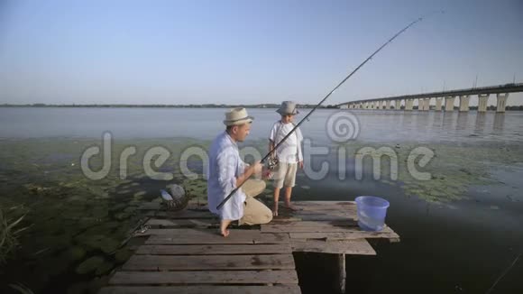 晚上钓鱼爸爸和他快乐的孩子坐在码头边一起看着纺棒钓鱼视频的预览图