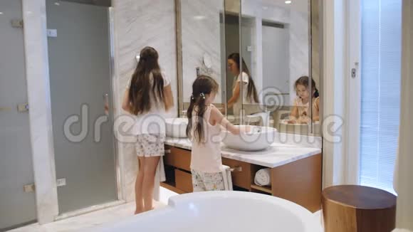 孩子们刷牙两个姐妹在浴室镜子前刷牙视频的预览图