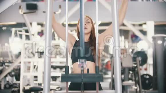 一位运动员女子在健身房训练坐着把杆拉到身体上训练二头肌视频的预览图