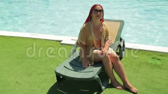 一位年轻的黑发女子正在游泳池附近的躺椅上晒太阳视频的预览图