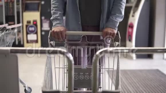 一个穿着蓝色衬衫和紫色裤子的男人把购物空车推到购物手推车上的镜头视频的预览图