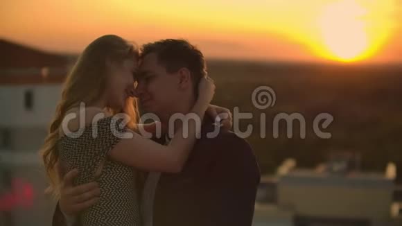 拥抱站在屋顶日落日落时的夏季屋顶一个男人和一个女孩在屋顶上进行了一次浪漫的约会视频的预览图