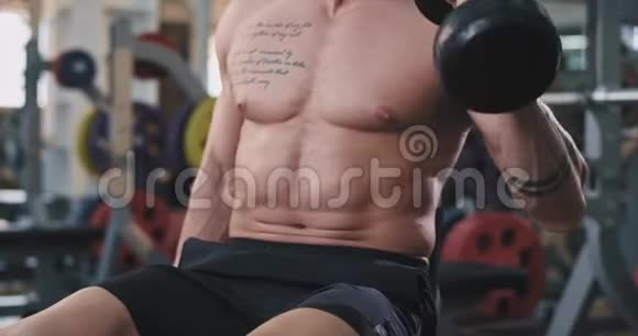 一个肌肉男在健身房里努力锻炼肱二头肌身体上有纹身的细节视频的预览图