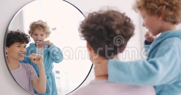 妈妈和儿子在浴室里刷牙看着镜子一起微笑视频的预览图