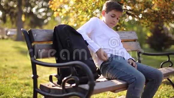 小男孩从口袋里拿出智能手机坐在公园长凳上的少年视频的预览图