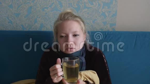 年轻女子病了坐在沙发上喝热茶视频的预览图
